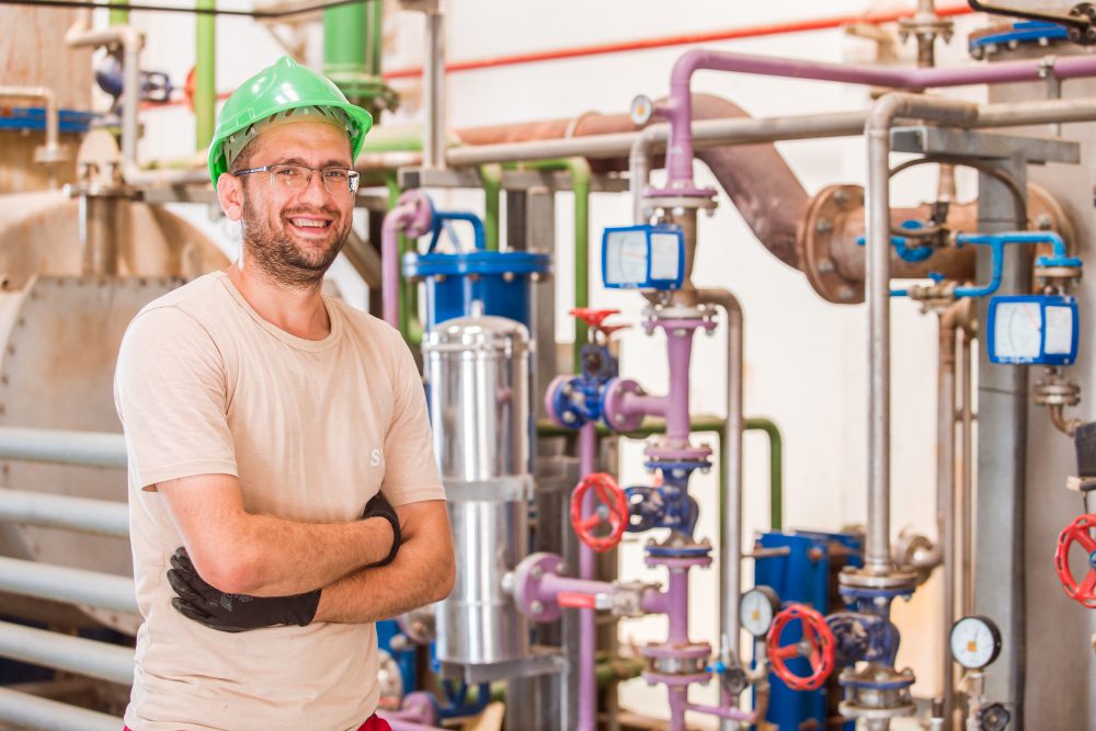 happy industry worker posing smiling inside factory with bars pipes around